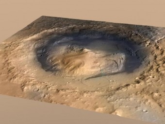 Visuale d’insieme del cratere Gale, il punto di atterraggio del rover Curiosity su Marte. All’interno del cratere è presente un rilievo alto 5.5 mila km che si chiama Monte Sharp. Il cerchio indica il punto d’approdo di Curiosity, la linea blu rappresenta il suo tragitto. Crediti: NASA/JPL