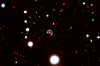 Image of the “Canarias Einstein ring”. In the centre of the picture, we can see how the source galaxy (the greenish-blue circle), which is further away “surrounds” the lens galaxy (red dot) almost completely. This phenomenon is produced because the strong gravitational field of the lens galaxy distorts the space-time in its neighbourhood, bending the paths of the light rays which come from the source galaxy. As they are almost perfectly aligned, the resulting image of the source galaxy is almost circular. Credit: Image made up from several images taken with the DECam camera on the Blanco 4m telescope at the Cerro Tololo Observatory in Chile.