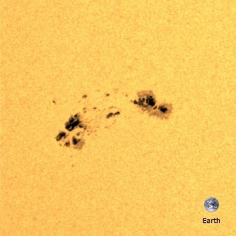 Una regione solare attiva vista dallo strumento HMI a bordo della sonda SDO della NASA. Le regioni più scure sono macchie solari, e corrispondono a zone in cui il campo magnetico della stella è più intenso. L’immagine della Terra è sovrapposta per confronto delle dimensioni. Crediti: MPS