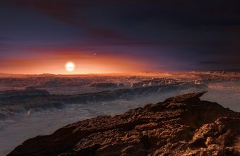 Rappresentazione artistica della superficie del pianeta Proxima b in orbita attorno alla nana rossa Proxima Centauri, la stella più vicina al Sistema solare. In alto a destra rispetto a quest’ultima, s’intravede anche la stella doppia Alpha Centauri AB. Crediti: ESO/M. Kornmesser