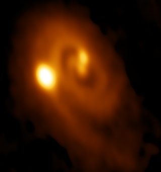 Immagine ottenuta ALMA del sistema L1448 IRS3B, con due giovani stelle verso il centro e una terza più lontana. La struttura a spirale del disco di gas e polveri che le circonda indica, secondo i ricercatori, instabilità gravitazionale. Credit: Bill Saxton, ALMA (ESO/NAOJ/NRAO), NRAO/AUI/NSF.